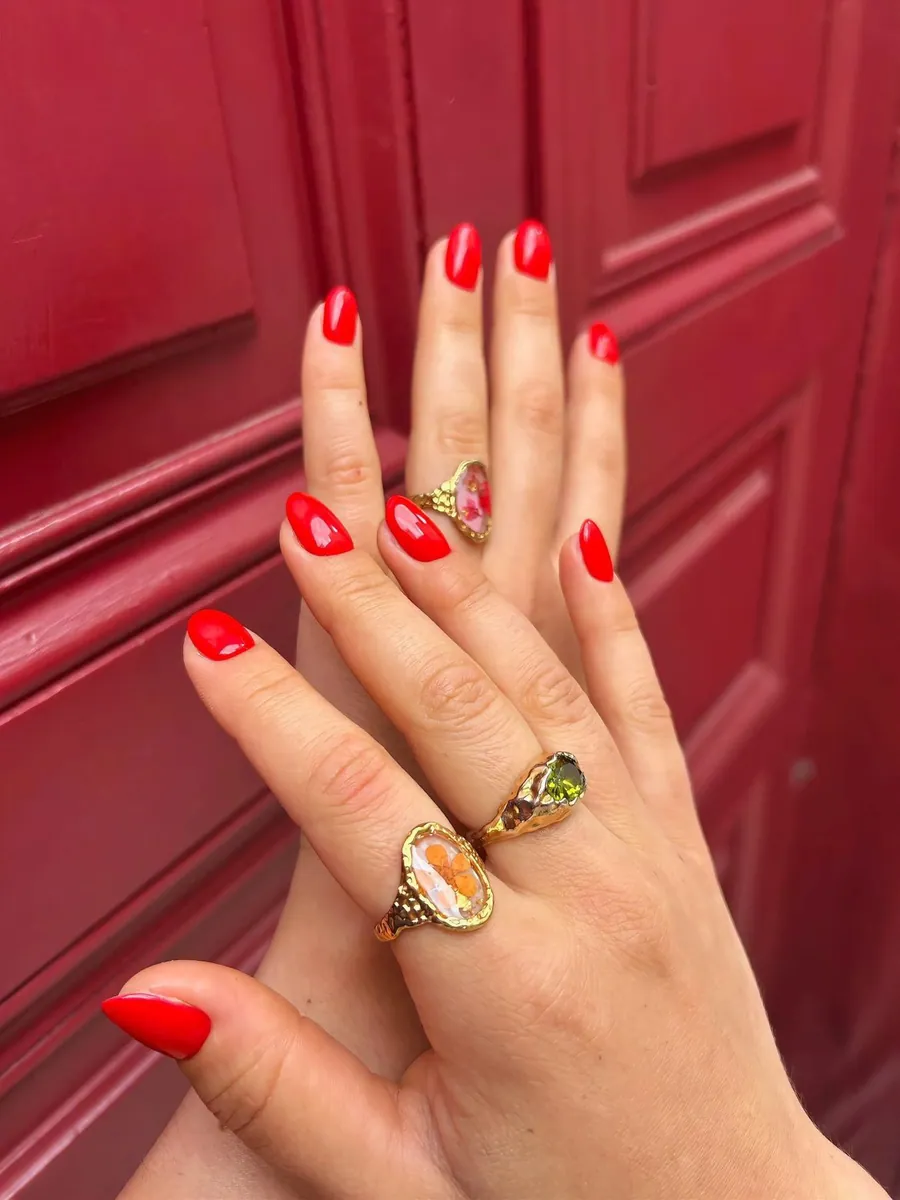 Pose de vernis rouge vif et brillant sur ongles en amande, avec bagues dorées